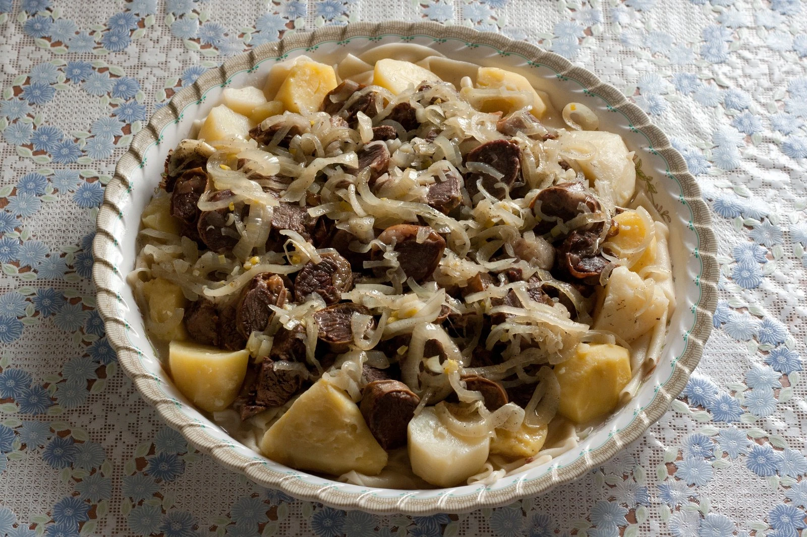 Grande vassoio di beshbarmak con carne di montone disossata su sfoglie di pasta all'uovo, irrorato di brodo e cipolla stufata