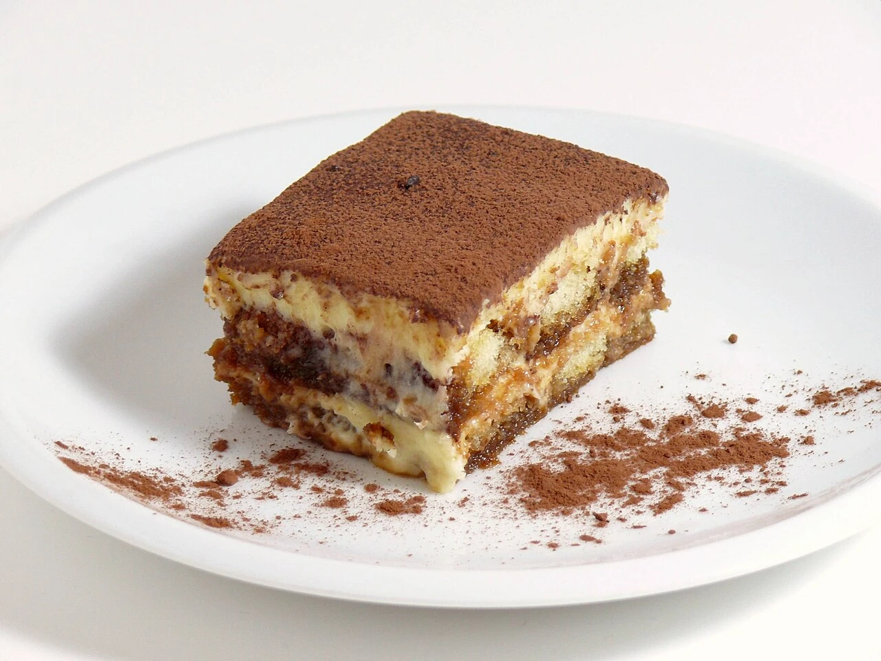 Fetta di tiramisù di Treviso con i savoiardi inzuppati nel caffè in sezione e la superficie spolverata di cacao amaro Fetta di tiramisù di Treviso con i savoiardi inzuppati nel caffè in sezione e la superficie spolverata di cacao amaro